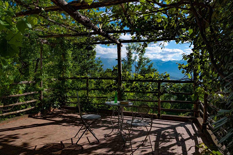 gazebo avvolto dal verde delle viti con tavolo e sedie per potersi rilassare guardando le montagne
